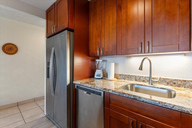 kitchen with brown cabinets, stainless steel appliances, light stone countertops, and a sink