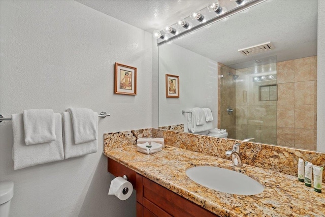 bathroom featuring a textured ceiling, visible vents, vanity, toilet, and tiled shower