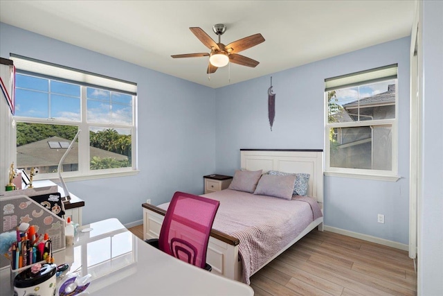 bedroom with light wood finished floors, multiple windows, a ceiling fan, and baseboards