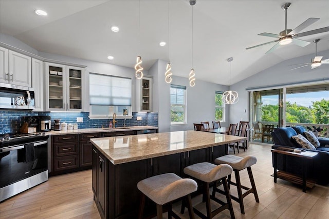 kitchen with a breakfast bar, a sink, stainless steel appliances, glass insert cabinets, and vaulted ceiling