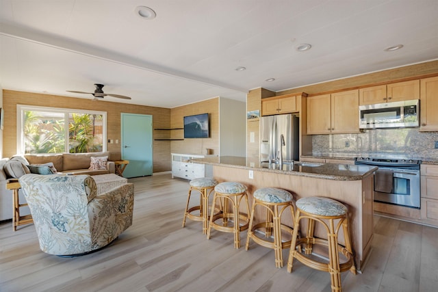 kitchen featuring a center island with sink, light wood-type flooring, light brown cabinetry, stone countertops, and stainless steel appliances