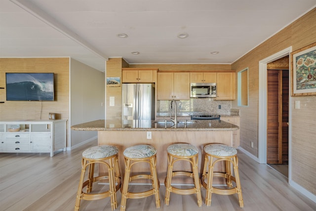 kitchen with light stone countertops, light wood-type flooring, stainless steel appliances, and light brown cabinetry