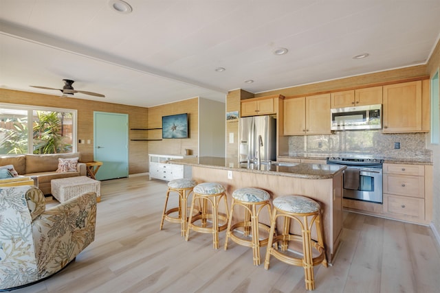 kitchen featuring an island with sink, light brown cabinetry, appliances with stainless steel finishes, light hardwood / wood-style floors, and light stone counters