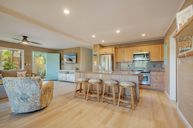 kitchen featuring light wood-type flooring, stainless steel appliances, a kitchen island with sink, and a breakfast bar area