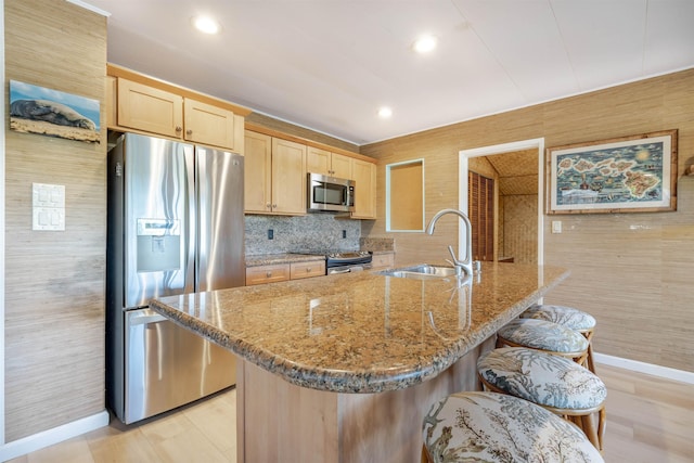 kitchen featuring appliances with stainless steel finishes, light brown cabinetry, light stone counters, a breakfast bar, and sink