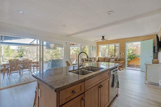 kitchen featuring dark stone counters, ceiling fan, sink, light hardwood / wood-style floors, and an island with sink