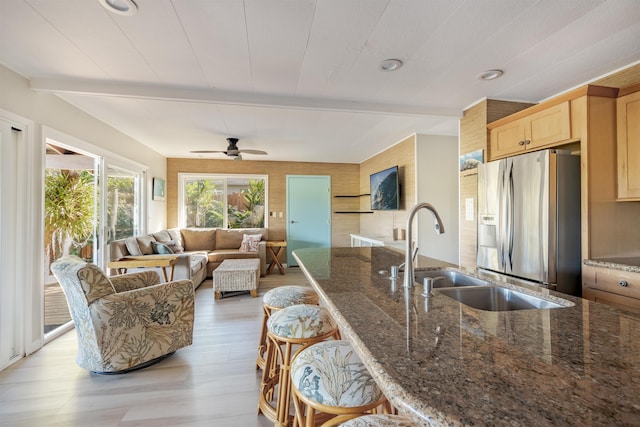 kitchen with a kitchen breakfast bar, sink, dark stone countertops, light wood-type flooring, and stainless steel fridge with ice dispenser