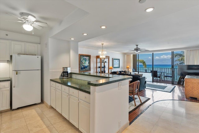 kitchen with a wall of windows, white cabinetry, white fridge, kitchen peninsula, and pendant lighting