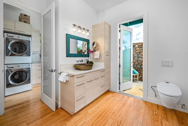 bathroom with french doors, vanity, wood-type flooring, stacked washer and dryer, and toilet