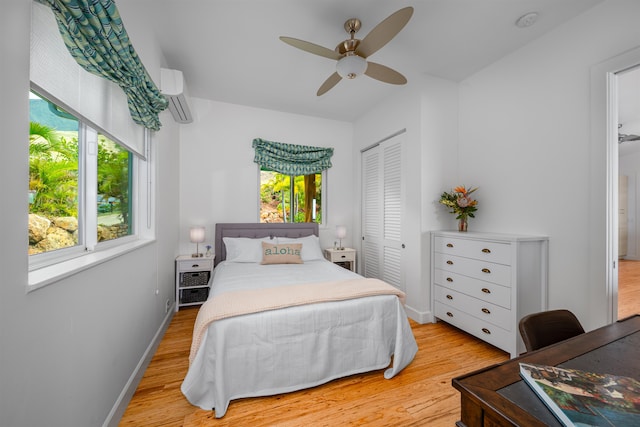 bedroom with a wall mounted AC, light wood-type flooring, a closet, and ceiling fan