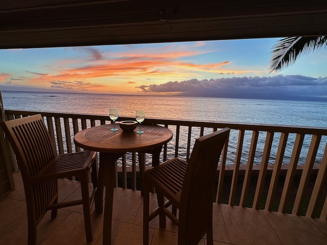 balcony at dusk featuring a water view