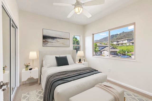 carpeted bedroom with baseboards, ceiling fan, a mountain view, and a closet