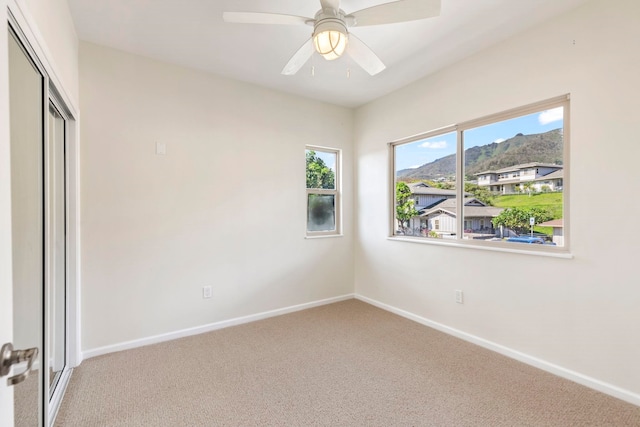 unfurnished bedroom featuring a closet, ceiling fan, a mountain view, light carpet, and baseboards