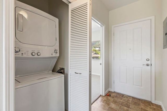 laundry room with baseboards, stacked washing maching and dryer, stone finish floor, and laundry area
