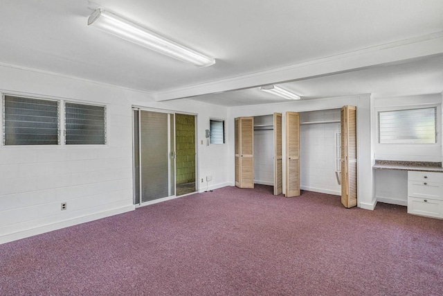 unfurnished bedroom with carpet floors, concrete block wall, two closets, built in study area, and baseboards