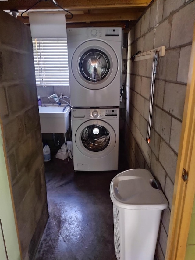 clothes washing area with stacked washer and dryer, concrete block wall, laundry area, and a sink