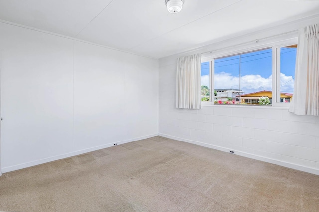 carpeted spare room with concrete block wall and baseboards