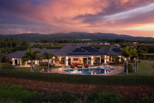 back house at dusk featuring a lawn, a mountain view, a patio area, and solar panels