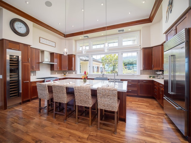 kitchen with a center island with sink, stainless steel appliances, beverage cooler, light stone countertops, and wall chimney range hood