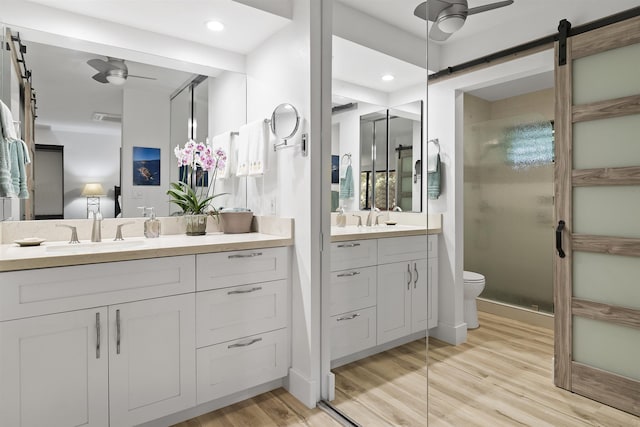 bathroom featuring a ceiling fan, toilet, wood finished floors, vanity, and a shower stall