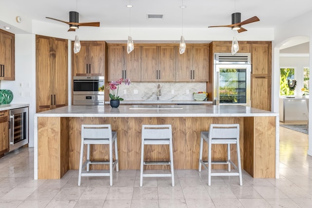 kitchen with a kitchen breakfast bar, wine cooler, ceiling fan, double oven, and a spacious island