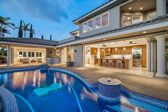 pool at dusk with a patio, area for grilling, and a bar