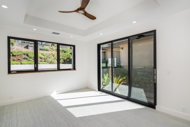 unfurnished room with a tray ceiling, light colored carpet, and ceiling fan