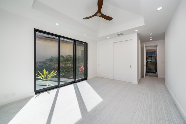 unfurnished bedroom featuring ceiling fan, access to exterior, a raised ceiling, light carpet, and a closet