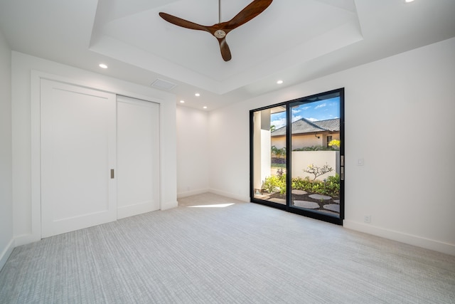 unfurnished bedroom with a closet, a tray ceiling, light carpet, and access to exterior