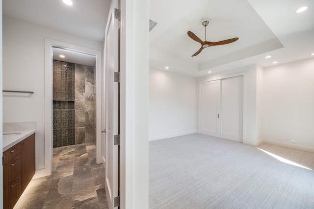 bathroom with a raised ceiling, vanity, tiled shower, and ceiling fan