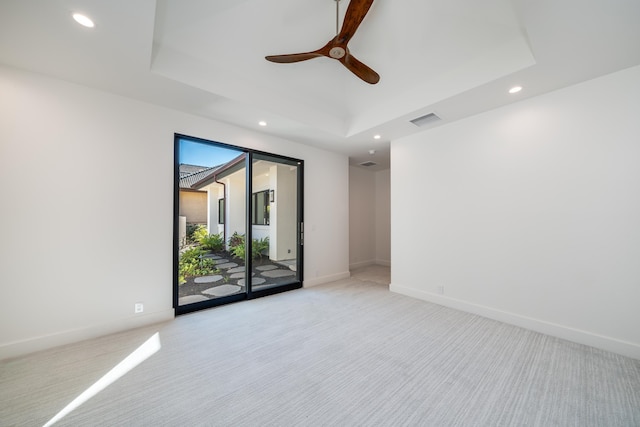 empty room with ceiling fan, light colored carpet, and a tray ceiling