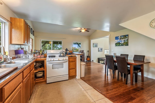 kitchen featuring ceiling fan, sink, light tile flooring, white gas stove, and vaulted ceiling