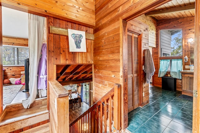 hallway with wood ceiling, dark tile flooring, lofted ceiling with beams, and wooden walls