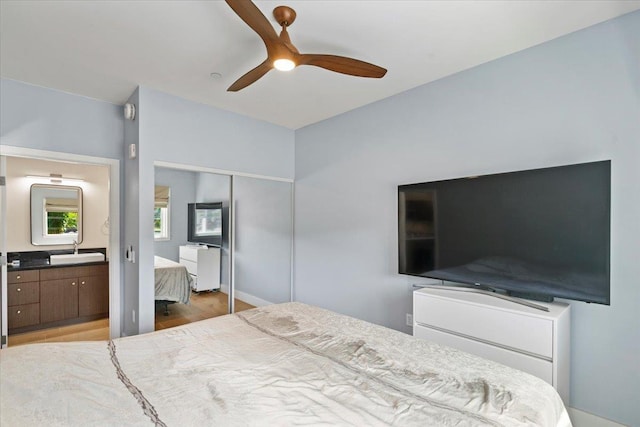 bedroom with ensuite bathroom, wood finished floors, a closet, a ceiling fan, and a sink