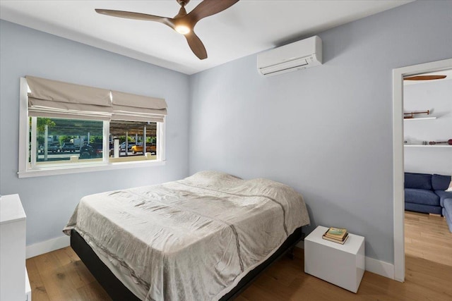 bedroom with a wall mounted air conditioner, baseboards, and wood finished floors