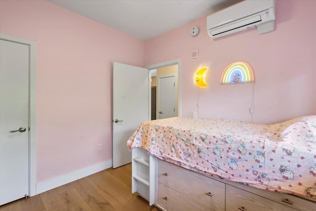 bedroom featuring light wood-style flooring, an AC wall unit, and baseboards