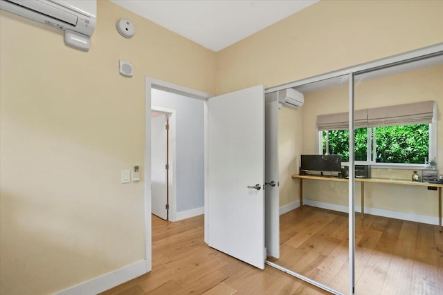 unfurnished bedroom featuring baseboards, wood-type flooring, and a wall mounted AC