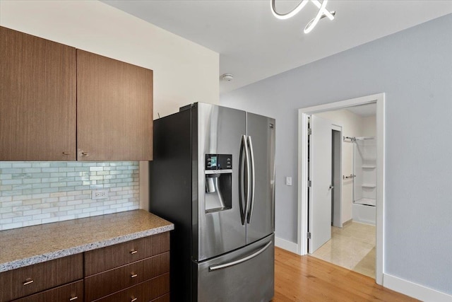 kitchen with baseboards, light wood finished floors, light countertops, stainless steel fridge, and tasteful backsplash