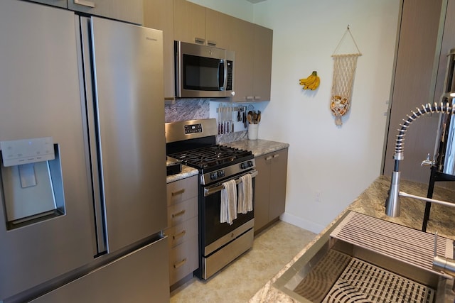 kitchen featuring light stone countertops, gray cabinets, stainless steel appliances, and tasteful backsplash