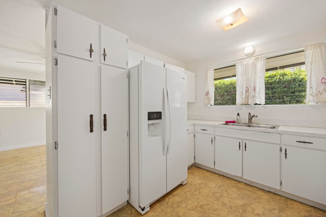 kitchen featuring white cabinets, a textured ceiling, white fridge with ice dispenser, and sink