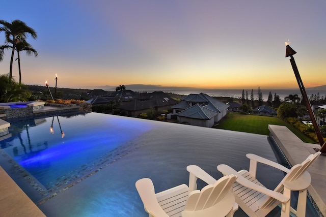 pool at dusk with an in ground hot tub and a water view