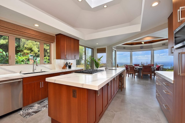 kitchen featuring a center island with sink, sink, a raised ceiling, appliances with stainless steel finishes, and tasteful backsplash