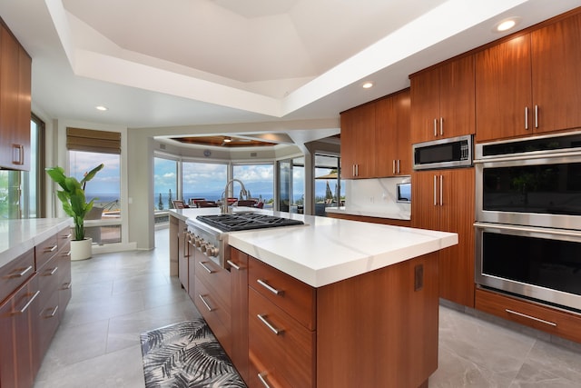 kitchen with a kitchen island, decorative backsplash, stainless steel appliances, a tray ceiling, and light tile patterned floors