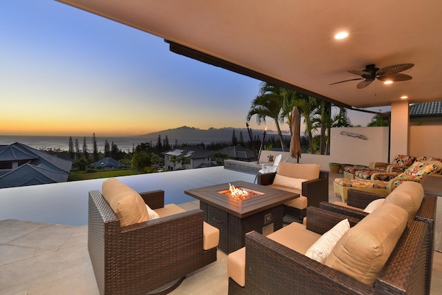 patio terrace at dusk with a water and mountain view, an outdoor living space with a fire pit, and ceiling fan