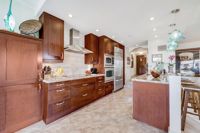 kitchen featuring pendant lighting, built in appliances, a kitchen breakfast bar, and wall chimney exhaust hood