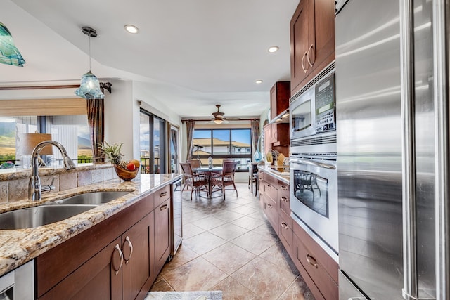 kitchen featuring ceiling fan, sink, hanging light fixtures, stainless steel appliances, and light stone counters