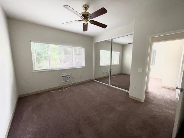 unfurnished bedroom featuring ceiling fan, a closet, dark colored carpet, and an AC wall unit