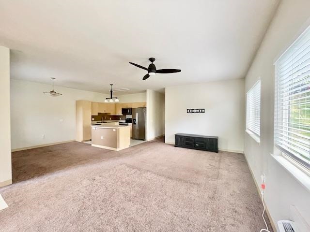 unfurnished living room with ceiling fan, light colored carpet, and sink