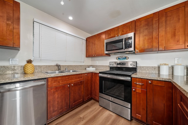 kitchen with stainless steel appliances, light hardwood / wood-style flooring, light stone counters, and sink