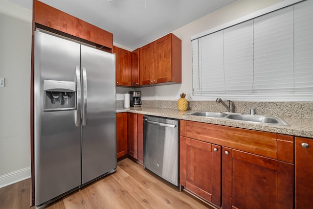 kitchen with appliances with stainless steel finishes, light hardwood / wood-style floors, sink, and light stone counters